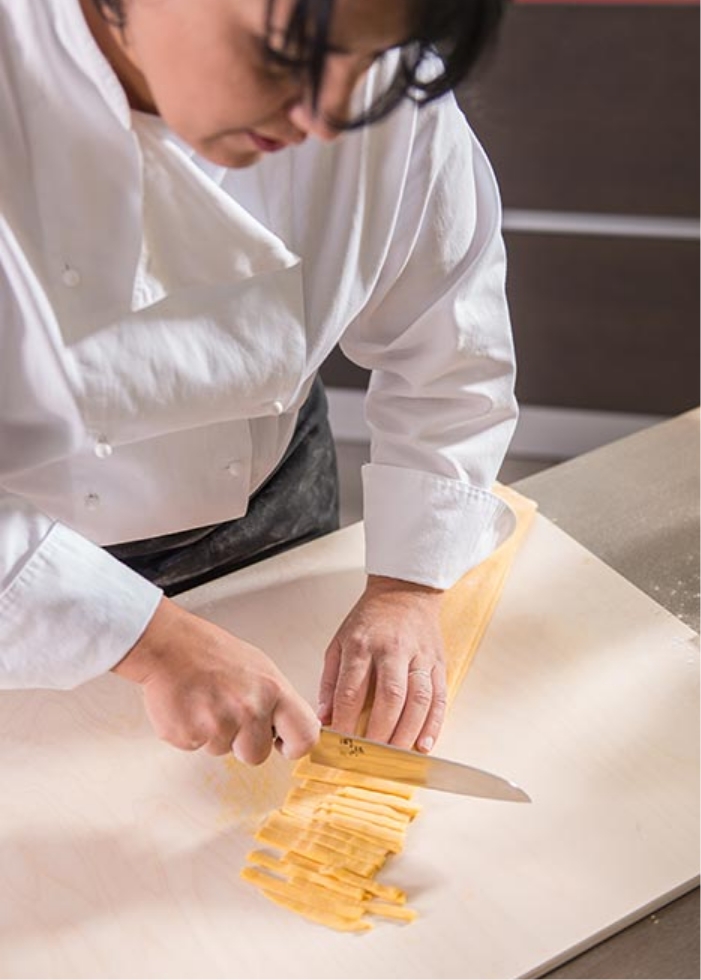 Antonella La Macchia, a Sicilian cook in Tuscany, skillfully cutting pasta on a cutting board.