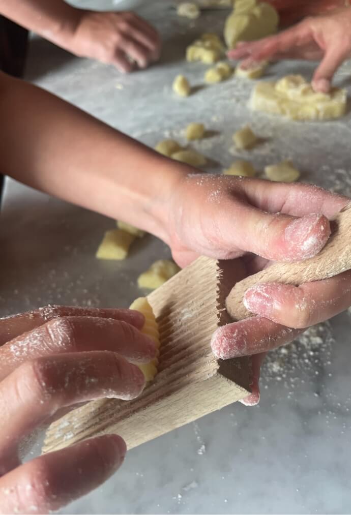 In a picturesque Tuscany farm stay, a person is skillfully using a wooden board to make pasta during a cooking class. Traditional Italian cooking at its finest!